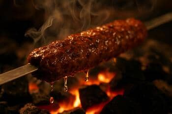Köz üzerinde kızaran kebap: parlak yağ damlaları ve duman
