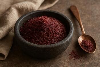 Koyu taş kasede toz sumak, yanında bakır kaşık ve keten örtü